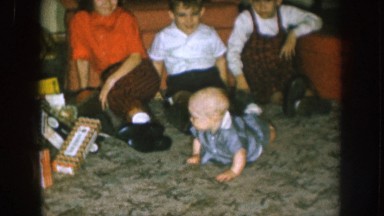 1957: three sitting children and a crawling baby play and pose for the camera in