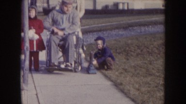 1957: Children Walking Down Sidewalk With Grandparents, Grandad in Wheelchair