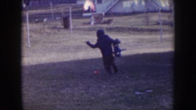 1957: little boy running outside with a big toy, stops to pick up another toy