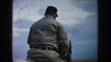 1953: Man in Khaki Outfit and Hat Rides Horse in Circles Through Field with Mountain Views