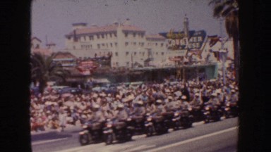 1952: large crowd of people lined on the side of a street while more go down the