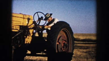 1953: man attempting to ride a yellow tractor in a barren field on a blue-sky