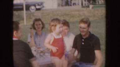 1955: little girl in red leotard standing on picnic bench surrounded by adults