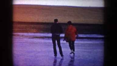 1953: a man and two women skate on an outdoor lake in an open space while dog