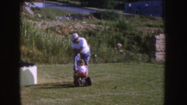 1955: father playing with kids and helping toddler ride tricycle in a backyard
