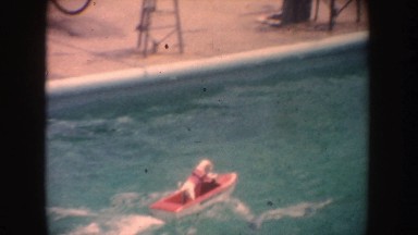 1962: Small Dog Riding Miniature Motorboat in Pool Pretending to Steer