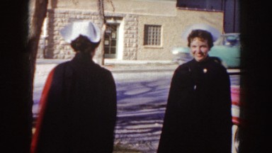 1955: Two Young Nurses Wearing Capes Standing Alongside a Red Car