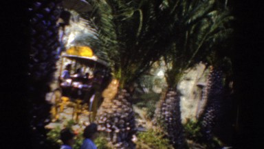 1952: horses and carriages wit people drive past palm trees next to women