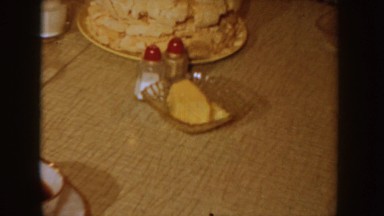 1955: cake being placed on a kitchen table with people sitting at table and