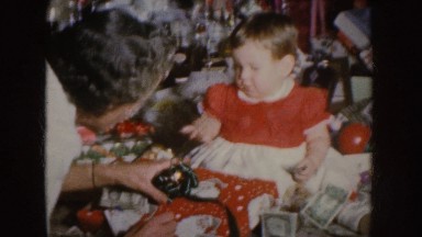 1955: Mother Assisting Baby to Unwrap Christmas Present with Money and Objects