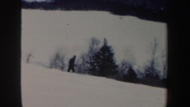 1962: skier skiing down a moderate slope in between conifers; skiers exiting