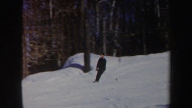 1962: man quickly skiing in snow down a mountain path in the forest on a sunny