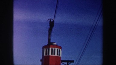 1962: Red and White Cable Car Ascending Mountain with Skier Underneath
