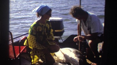 1969: Woman Wearing Caftan on Boat with Man Reeling in Fish