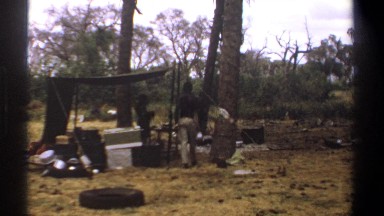 1969: Two Individuals Standing Under Covered Shelter Near Embankment in Kenya