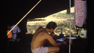 1969: man in tent messing with a machine next to a car SUDAN