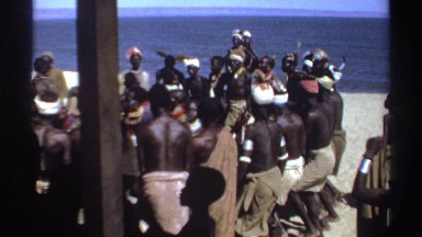 1969: a group of people dancing in a circle near the shore line on a sunny day
