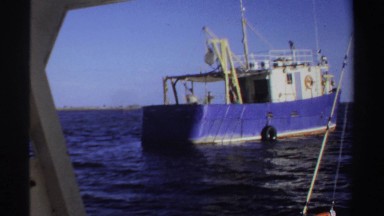 1969: from vantage of boat, another fishing vessel moves away; man on boat with