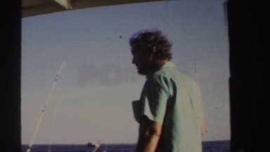 1969: man in a boat smoking cigarette pointing hand on something and fishing.
