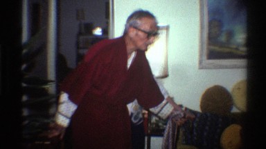 1975: older woman in a christmas sweater helping an elderly man in a red robe to