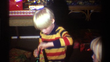 1975: golden haired, brightly clothed children open wrapped presents in home