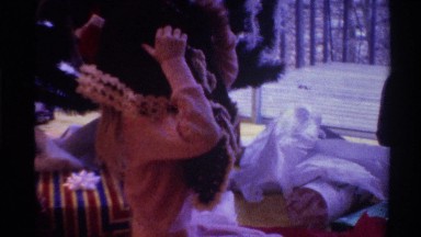 1975: girl tries putting on a poncho and her mother helps while they all sit in