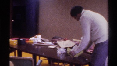 1975: man clears papers off table, followed by view of two children, the second