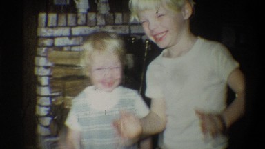 1973: two children smiling next to a fire place keeping warm NEW YORK