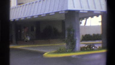 1973: hotel awning over a drive through with foliage and greenery, a guest pulls