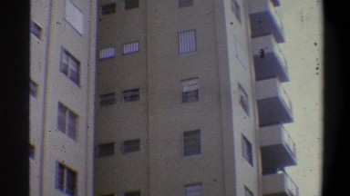 1973: a shaky camera shot of a tall and light brown residential building on a