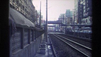 1982: Electric Train Running on Track with Vehicles Moving on Road Side