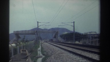 1982: dark train travels away from mountains on tracks parallel to road with