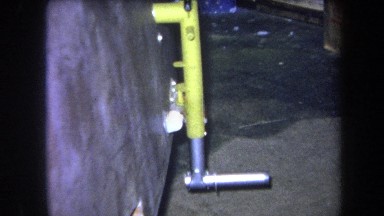 1964: Yellow Metal Rod Installed in Cement Wall with Silver L-Shaped Component