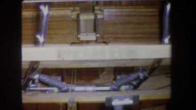 1965: incomplete wooden base of what appears to be a boat sits in a dimly lit