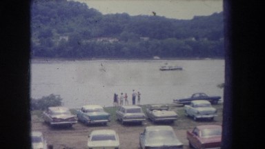 1968: a boat moving through the water in the lake with a bank where vehicles