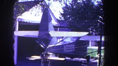 1969: small plane marked n2228 is parked outside of garage by worktable, tree