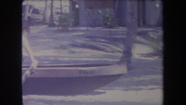 1969: people on a park-like setting with a boy climbing into an outrigged canoe;
