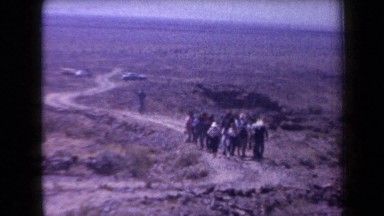 1958: a group of men and women walking along a track through an arid landscape