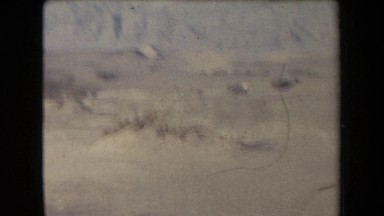 1958: two men visible at the base of a mountain valley with a few people in the