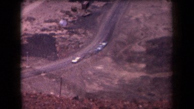 1958: Five Cars in Distance, Two Men Walking, Desert Mountain Background