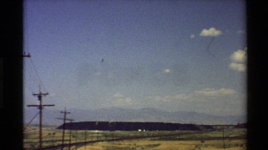 1980: panorama of a factory by the roadside below a mountain in the desert