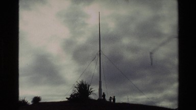 1981: darkened sky with large metal post and guy wires; small harbor with man