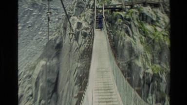 1982: man on old rope bridge over rushing waters NEW ZEALAND