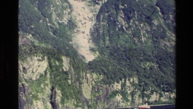 1982: view of the side of a large mountain, covered in greenery NEW ZEALAND