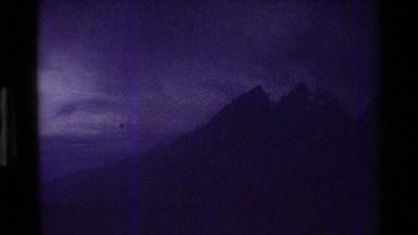 1980: cars moving through a valley towards very steep mountain peaks with snow
