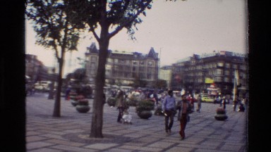 1982: people walking in a city in a brick square with flags waving