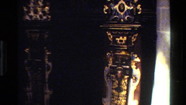 1982: ornamental panel has small face centered between profiles of curved-beak