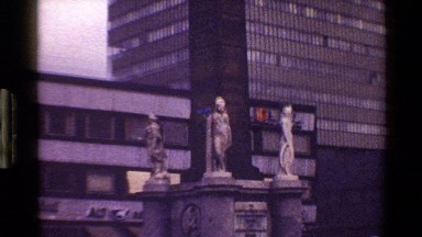 1983: three stone statues stand before a large skyscraper and other buildings