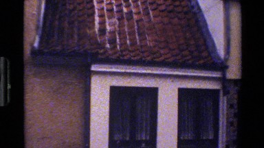 1983: black bird lands on ledge of roof as camera pans down to window. DENMARK