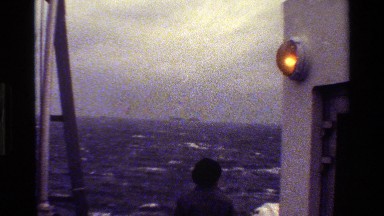 1983: man on boat looking out over rough seas to an isle DENMARK